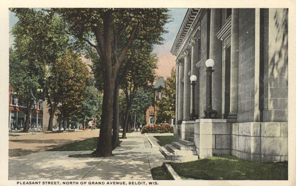 Colorized postcard view down sidewalk along tree-lined street in the central business district. On the right is a large marble building, and on the left side of the street are storefronts. Caption reads: "Pleasant Street, North of Grand Avenue, Beloit, Wis."