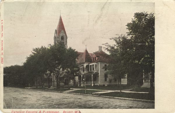 Colorized postcard view from street of the Catholic Church and Parsonage on a tree-lined street in a residential neighborhood. Caption reads: "Catholic Church and Parsonage, Beloit, Wis."