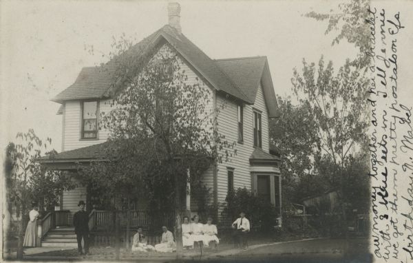 Photographic postcard view of the exterior of a house with a family posing in front.