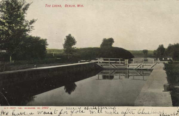 Colorized postcard view of a lock on the Fox River. Caption reads: "The Locks, Berlin, Wis."
