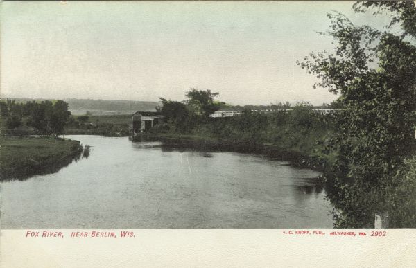 Colorized elevated view of the Fox River, with a boathouse and a road in the background on the right. Caption reads: "Fox River, near Berlin, Wis."