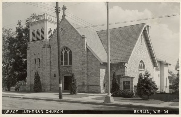 Photographic postcard of an exterior view from the street of a stone church. Caption reads: "Grace Lutheran Church, Berlin, Wis."