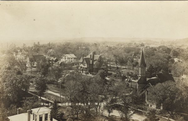 Elevated photographic postcard view of Black River Falls. There is a large building in the center with a large lawn. On the right is a church. Caption reads: "Black River Falls, Wis."