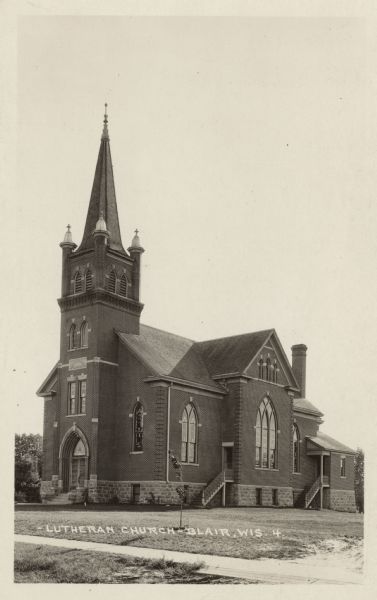 An exterior view of a brick church with arched stained glass windows and a steeple. Stairs leading to the front and 2 side entrances.