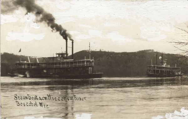 Photographic postcard view of two steamboats on the Wisconsin River. Tree-covered bluffs are on the opposite shoreline. The steamboat on the left is the "Grand," and the one on the right is the "Rapids." Caption reads: "Steamboats on Wisconsin River, Boscobel, Wis."