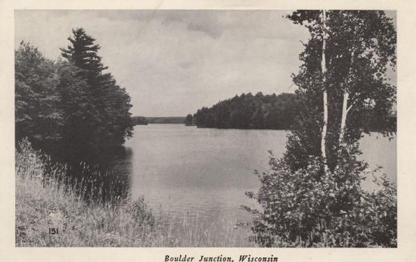 Photographic postcard view of Boulder Lake surrounded by trees. Caption reads: "Boulder Junction, Wisconsin."