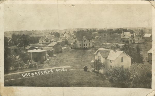 Elevated view of Brownsville featuring dwellings, gardens, sheds and a school. Caption reads: "Brownsville, Wis."