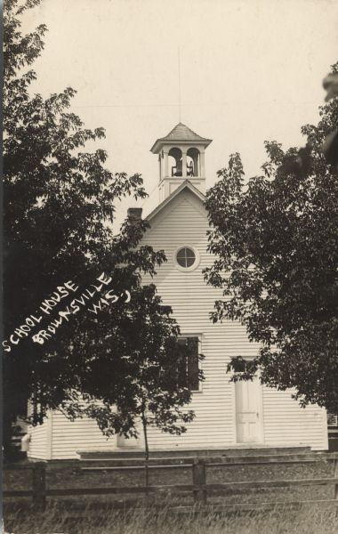 Photographic postcard view of the exterior of the schoolhouse. A fence is in front, and the schoolhouse has an open belfry. Caption reads: "School House, Brownsville, Wis."