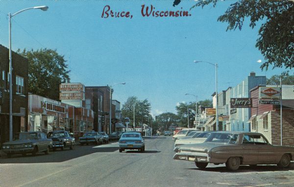 Color of Main Street. A Ben Franklin store, bank and Texaco Station are on the left. The right side is lined with bars. Cars are parked along both sides of the street. Caption reads: "Bruce, Wis."