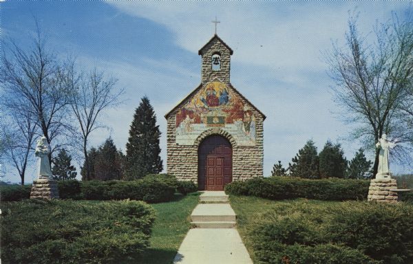 Color postcard view of a chapel with a fresco on the front. Statues of a Madonna and child and St. Francis are on the lawn.