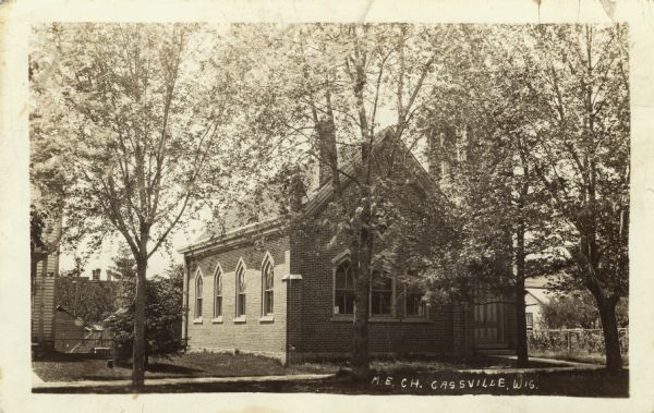 Photographic postcard view of a M.E. Church. The trees are in bloom. Caption reads: "M.E. Church, Cassville, Wis."