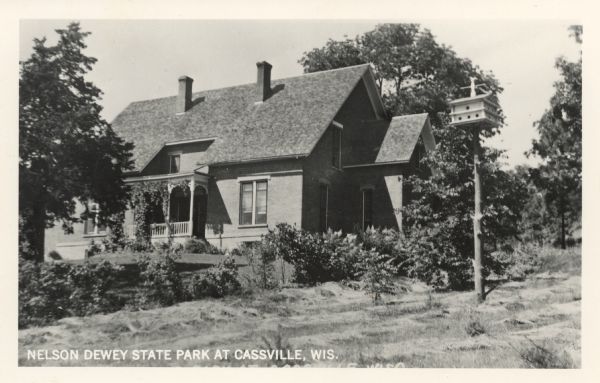 Photographic postcard view of the Nelson Dewey home at Nelson Dewey State Park. A birdhouse is in the foreground on the right. Caption reads: "Nelson Dewey State Park at Cassville, Wis."