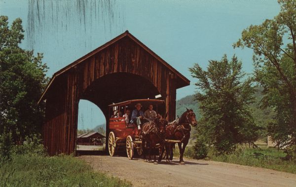 Color postcard of a covered bridge at Stonefield Village with a horse bus passing through it.