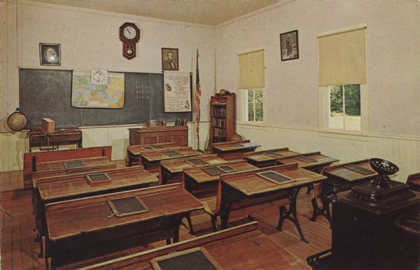 Color postcard of the classroom of the Muddy Hollow School at Stonefield. Slate tablets are on the desks.
