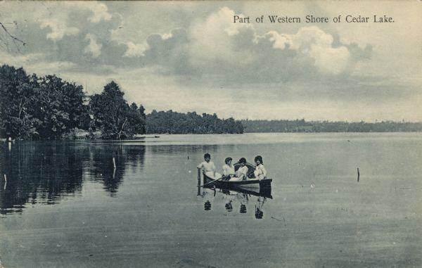 Hand-colored view of four women in a rowboat on Cedar Lake. One of the women is leaning her elbow on a post sticking out of the water. The tree-lined shoreline is in the background. Caption reads: "Part of Western Shore of Cedar Lake."