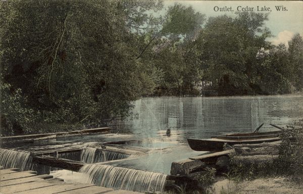 Hand-colored view of the Cedar Lake outlet with a wooden rowboat tied up at the bank above the outlet. Caption reads: "Outlet; Cedar Lake, Wis."