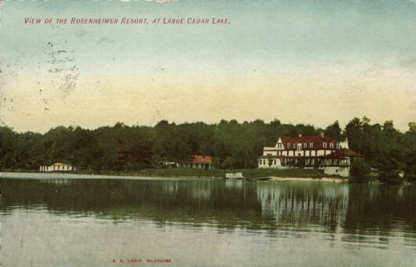 Hand-colored view of Rosenheimer Resort from across Big Cedar Lake. The resort has a large main building with a wrap-around porch, and there is a dock and a small beach. Caption reads: "View of the Rosenheimer Resort, at Large Cedar Lake."