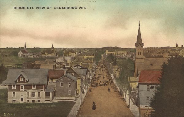 Hand-colored bird's-eye view down the center of a main street in Cedarburg. Horse and buggy traffic is in the street, with dwellings and buildings on the left and right, and at least three church buildings on the right and in the background. Caption reads: "Birds [sic] Eye View of Cedarburg, Wis."