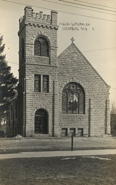 Photographic postcard of English Lutheran (now Advent Lutheran) Church, which is a stone building with a bell tower and an arched stained-glass window. Caption reads: "English Lutheran Ch., Cedarburg, Wis."