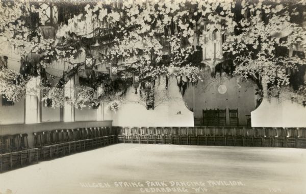 Interior view of the Hilgen Spring Park Dancing Pavilion. Chairs are along the walls, and flowers are hanging from the ceiling.