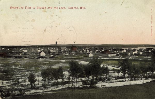 Hand-colored photomechanical view of Chetek. Chetek Lake is in the background on the right. The water tower is in the center. Caption reads: "Bird's-Eye View of Chetek and the Lake, Chetek, Wis."