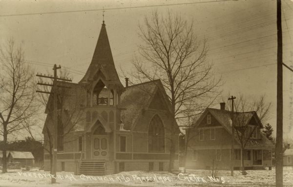 Exterior view of the Presbyterian Church and parsonage. A bell tower is over the front entrance of the church. Caption reads: "Presbyterian Church and Parsonage, Chetek, Wis."