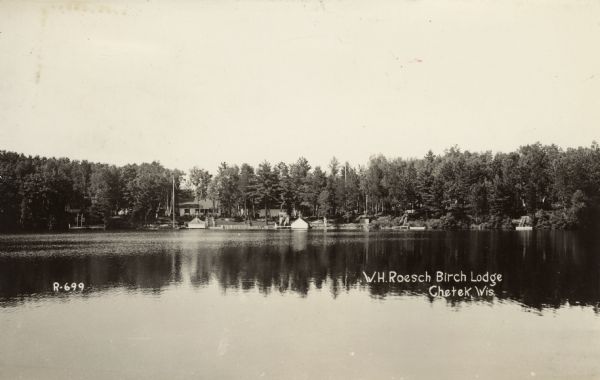 View across water towards the W.H. Roesch Birch Lodge on Lake Chetek. Docks and boathouses are along the shoreline. Caption reads: "W.H. Roesch Birch Lodge, Chetek, Wis."
