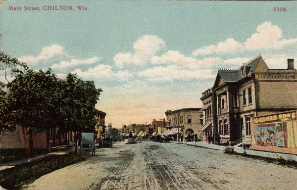 Hand-colored postcard view of the businesses along Main Street. Buggies are parked on the left. There is a circus poster on the right. Caption reads: "Main Street, Chilton, Wis."