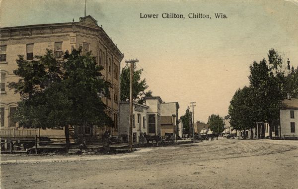 Hand-colored street view of a business district. There is a three-story brownstone on the left, and horses and carts are in the street. Caption reads: "Lower Chilton, Chilton, Wis."