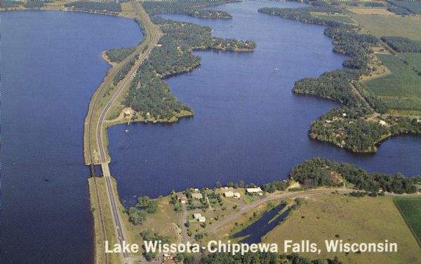 Color photograph of an aerial view of Lake Wissota looking east on Highway 29. Many resorts are in the area. Lake Wissota is one of the largest man-made lakes in the United States. Caption reads: "Lake Wissota - Chippewa Falls, Wisconsin."