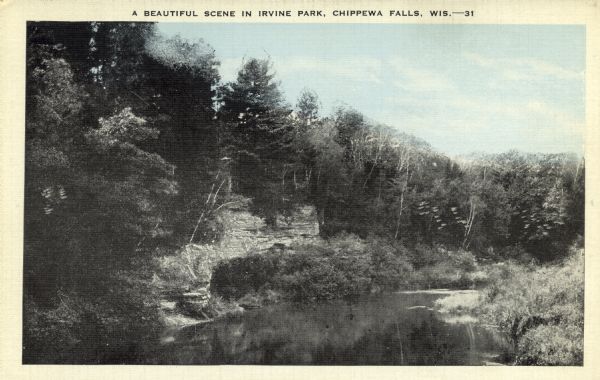 A tree-lined rock face next to Duncan Creek in Irvine Park in Chippewa Falls. Caption reads: "A Beautiful Scene in Irvine Park, Chippewa Falls, Wis."