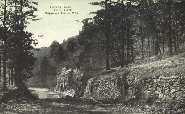 View down tree-lined "lovers' lane" on a hill along a stone wall and rock outcroppings in Irvine Park. Caption reads: "Lovers' Lane, Irvine Park, Chippewa Falls, Wis."