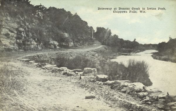 A curving, rutted dirt road between a rock wall at Duncan Creek in Irvine Park (probably the "Bear Cage Road"). Caption reads: "Driveway at Duncan Creek in Irvine Park, Chippewa Falls, Wis."