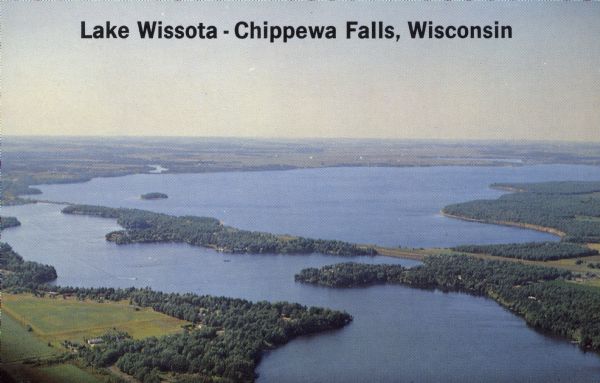 Aerial view, looking northwest, three miles east of Chippewa Falls, Wisconsin. Big Lake Wissota is seen across from Highway 29 in this color postcard, with Little Lake Wissota in the foreground. Caption reads: "Lake Wissota-Chippewa Falls, Wisconsin."