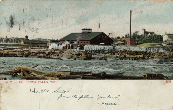 Colorized view of Big Mill, a lumber sawmill on the Chippewa river, next to a churning rapids. In the foreground are loose logs, whitewater, river boulders and an overflowing dam that is channeling logs from the river into the sawmill. In the background on the right is the Notre Dame church on a hill. On the left is part of the downtown. Caption reads: "Big Mill, Chippewa Falls, Wis."