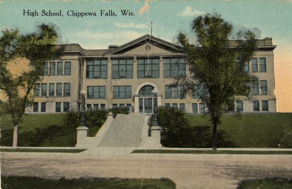 Hand-colored postcard view from across street towards the Chippewa Falls High School on North Bridge Street. Caption reads: "High School, Chippewa Falls, Wis."