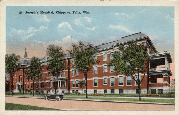 Color postcard view across street towards the St. Joseph's Hospital. An automobile is parked at the curb in front. Caption reads: "St. Joseph's Hospital, Chippewa Falls, Wis."