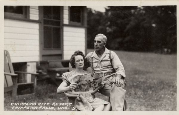Photographic postcard view of a man and woman sitting in an Adirondack chair at the Chippewa City Resort. Caption reads: "Chippewa City Resort, Chippewa Falls, Wis."