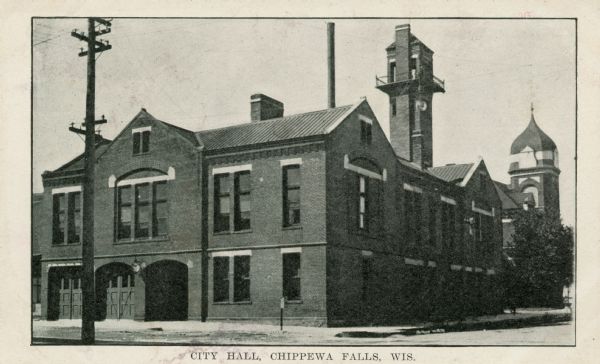 View from street of Chippewa Falls city hall. On the left are garage doors for fire engine storage, and a watch tower is at upper right.  Another building with a rounded steeple top is on the far right. Caption reads: "City Hall, Chippewa Falls, Wis."
