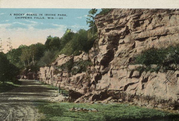 Colorized view of a rutted dirt road next to a rock face in Irvine Park. Caption reads: "A Rocky Scene In Irvine Park, Chippewa Falls, Wis."