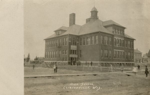 Black and white photographic postcard of the high school. Children are standing outdoors in front. Caption reads: "High School, Clintonville, Wis."