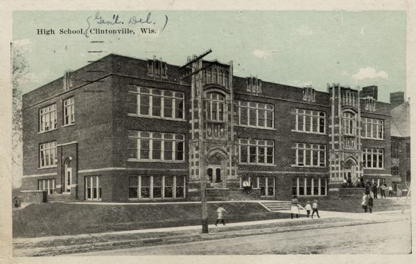 View from street towards the high school. There are children on the sidewalks in front of the building. Caption reads: "High School, Clintonville, Wis."