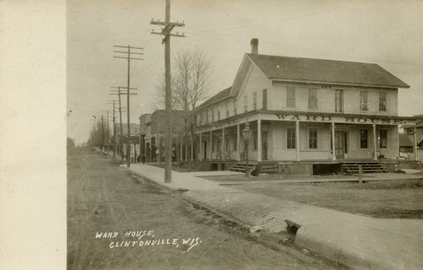 Black and white postcard view looking up unpaved road and sidewalk towards the Ward House. Caption reads: "Ward House, Clintonville, Wis."