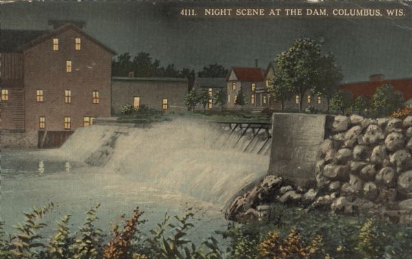 Color postcard view from shoreline looking towards of the dam on the Crawfish River. Buildings are on the opposite shoreline. Caption reads: "Night Scene at the Dam in Columbus, Wis."