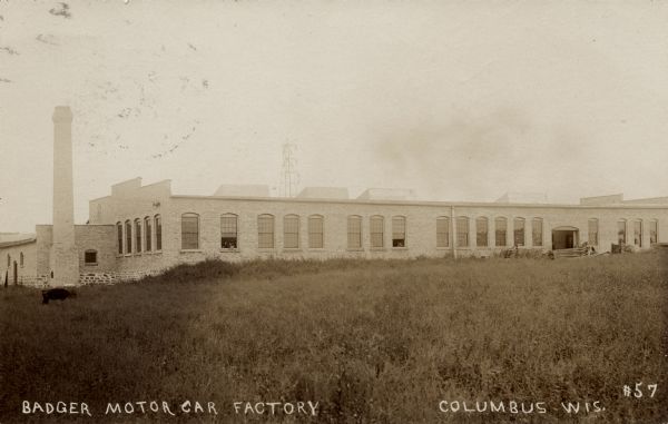 Photographic postcard view looking across field towards of the Badger Motor Car factory. Caption reads: "Badger Motor Car Factory, Columbus, Wis."