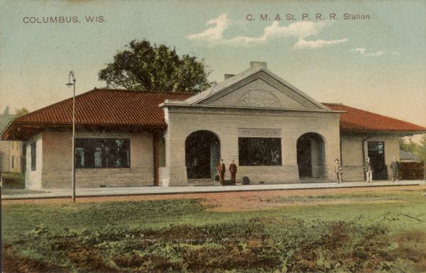 Color postcard of the Chicago, Milwaukee, St. Paul Railroad station. Five men are standing on the platform. Caption reads: "Columbus, Wis." and "C.M. & St. P. R. R. Station."