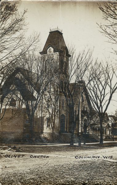 Black and white photographic postcard view from street of Olivet Church. Caption reads: "Olivet Church, Columbus, Wis."