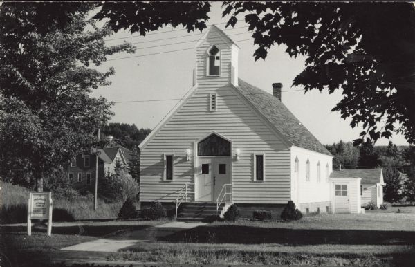 Photographic postcard of a white painted, wood frame Immanuel Lutheran Church. Sign out front. Sent Sept. 15, 1965, to thank visitors from Eau Claire for coming to the church, and inviting them to come again.