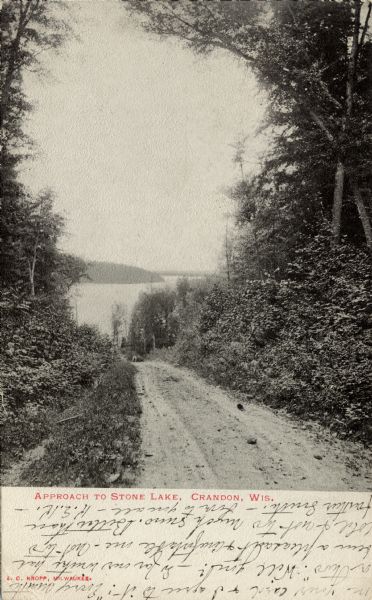 Photographic postcard showing dirt road leading to the shoreline of Stone Lake near Crandon. Caption reads: "Approach to Stone Lake, Crandon, Wis."
