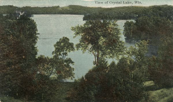 Elevated view from hill of Crystal Lake, with wooded shoreline. Caption reads: "View of Crystal Lake, Wis."